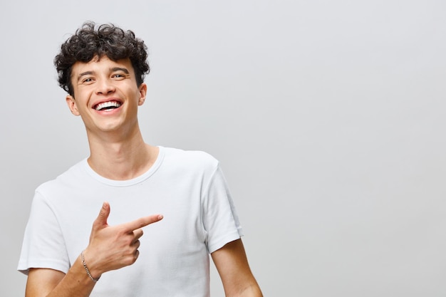 Un joven sonriente señalando con entusiasmo contra un fondo gris claro con una camiseta blanca casual