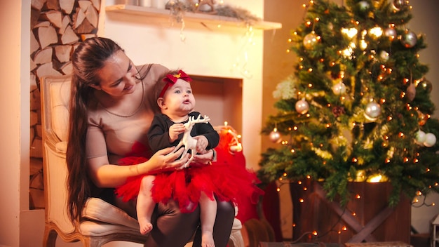 Una joven sonriente sentada en una silla con su pequeña hija en el estudio de Navidad