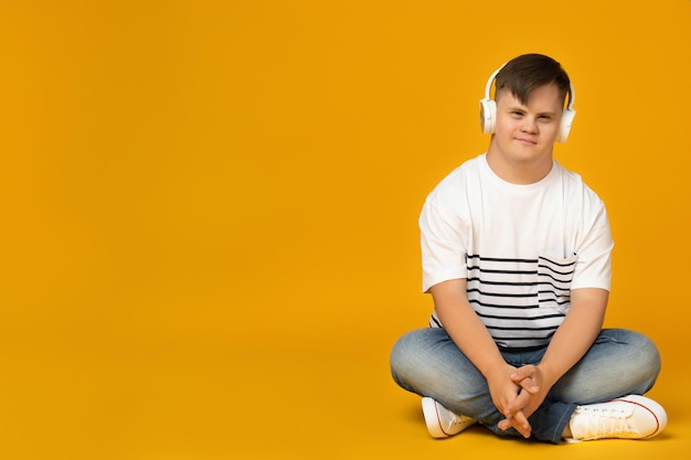 Un joven sonriente con síndrome de Down con gafas escuchando música con auriculares en lugar de texto