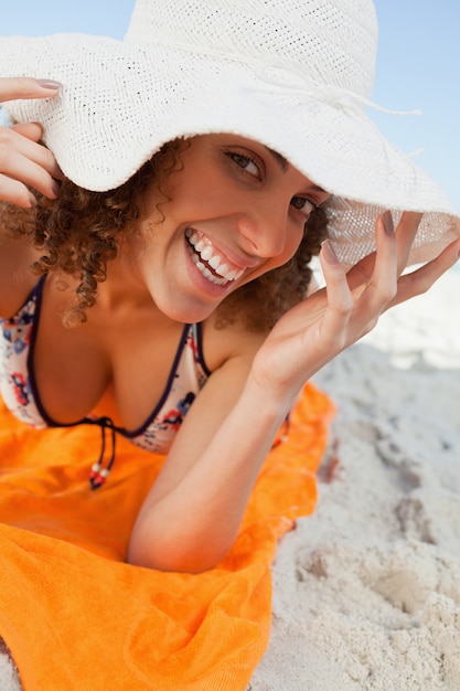 Joven sonriente, sosteniendo el borde del sombrero mientras está acostado