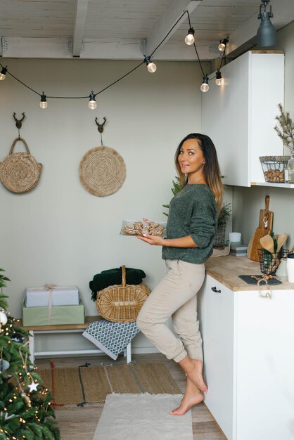 Una joven sonriente sostiene un plato de galletas de Navidad de jengibre en sus manos en la cocina