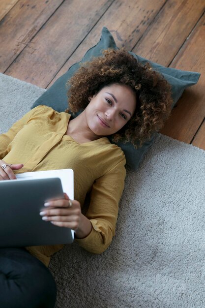 Una joven sonriente tirada en el suelo en casa con una laptop