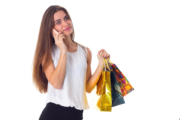 Joven sorprendida con blusa blanca y falda sosteniendo bolsas de compras y hablando por teléfono