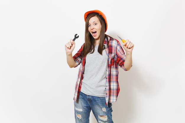 Joven sorprendida hermosa mujer en casco naranja de construcción protectora con destornillador de juguete y llave aislada sobre fondo blanco. Instrumentos para la renovación de la habitación del apartamento. Reparar el concepto de hogar.