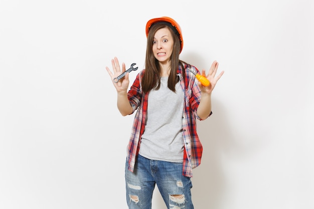 Joven sorprendida hermosa mujer en casco naranja de construcción protectora con destornillador de juguete y llave aislada sobre fondo blanco. Instrumentos para la renovación de la habitación del apartamento. Reparar el concepto de hogar.