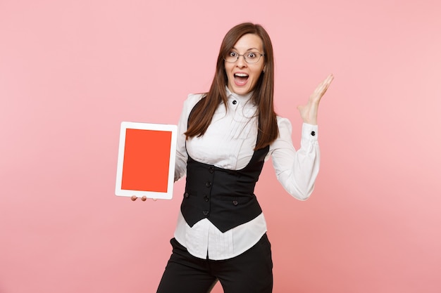 Foto joven sorprendida mujer de negocios en vasos mantenga tablet pc con pantalla vacía en blanco extendiendo las manos aisladas sobre fondo rosa. jefa. riqueza de carrera de logro. copie el espacio para publicidad.