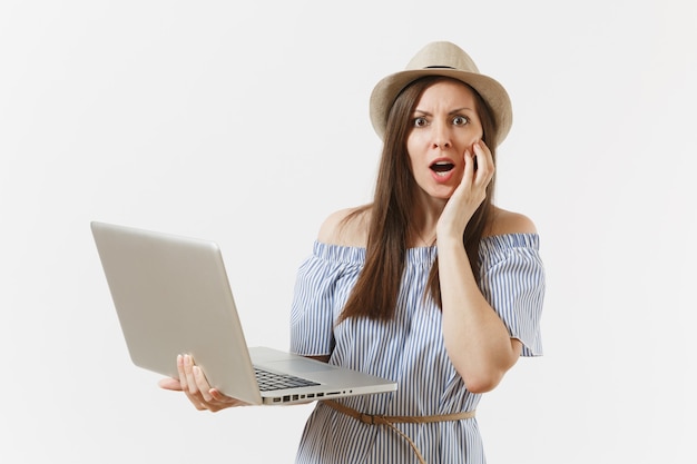 Joven sorprendida en vestido azul, sombrero trabajando en equipo portátil moderno aislado sobre fondo blanco. Personas, negocios independientes, estilo de vida, concepto de compras en línea. Oficina móvil. Publicidad.