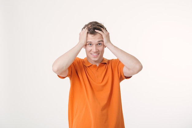 Joven sorprendido con cabello castaño sonriendo y sosteniendo sus manos en la cabeza