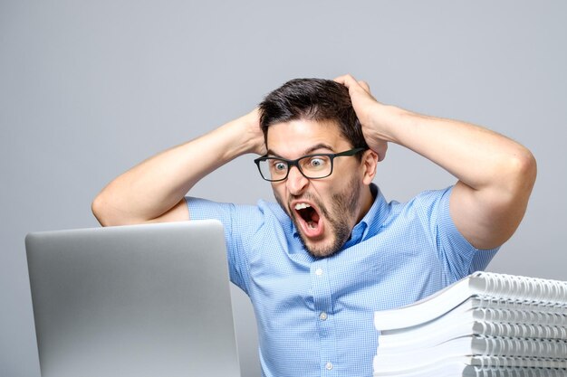 Joven sorprendido en camisa azul usando laptop