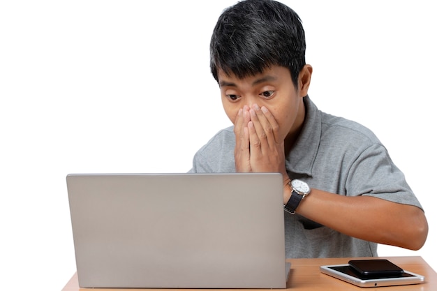 Joven sorprendido está navegando en su computadora portátil con teléfono inteligente y tableta en el escritorio aislado