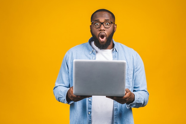 Joven sorprendido hombre africano de pie y usando la computadora portátil