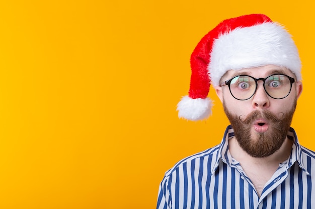 El joven sorprendido Santa Claus cierra la boca con sorpresa mientras está en una pared amarilla. El concepto de felicitaciones por el año nuevo y la Navidad.