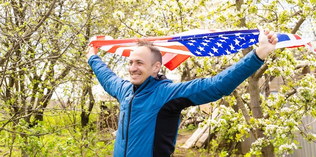 Joven sosteniendo la bandera nacional americana al cielo con las dos manos.