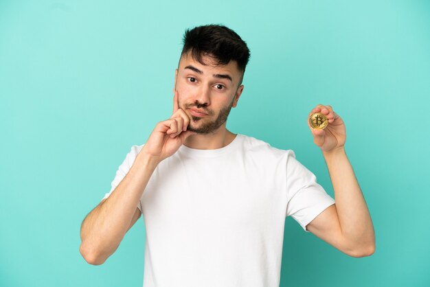 Joven sosteniendo un Bitcoin aislado sobre fondo azul pensando en una idea