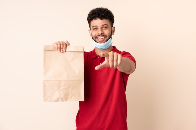 Joven sosteniendo una bolsa de comida para llevar le señala con el dedo con una expresión de confianza