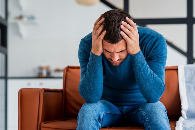 Joven sosteniendo la cabeza en las manos en el sofá