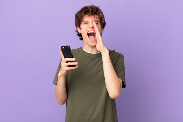 Joven sosteniendo una celda sintiéndose feliz, dando un gran grito con las manos al lado de la boca