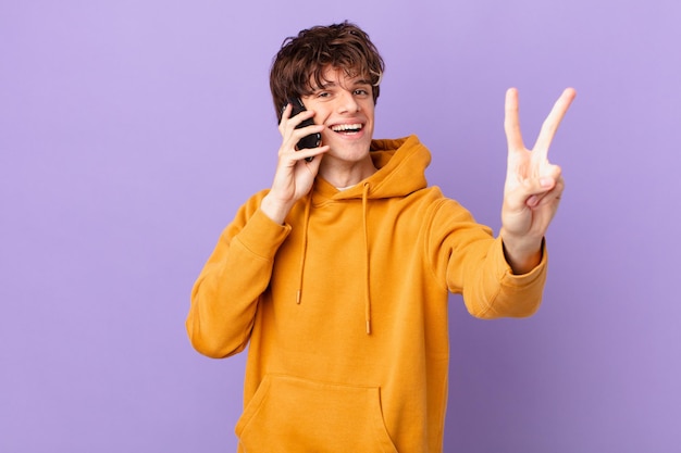 Joven sosteniendo una celda sonriendo y luciendo feliz, gesticulando victoria o paz