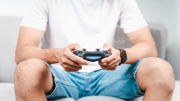 joven sosteniendo un controlador de joystick jugando videojuegos sentado en el sofá en casa