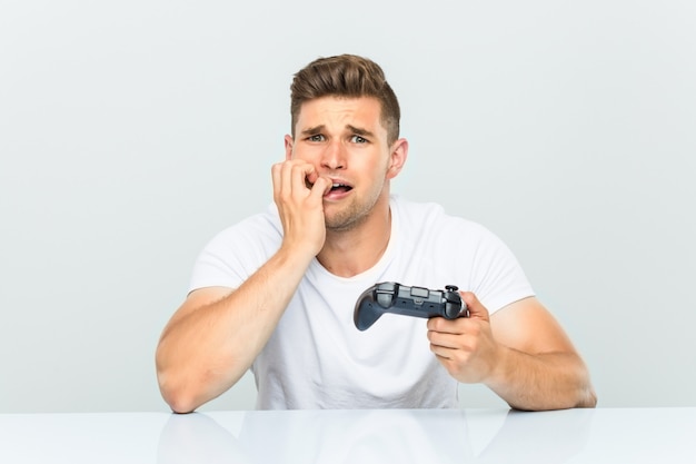 Joven sosteniendo un controlador de juego mordiendo las uñas, nervioso y muy ansioso.