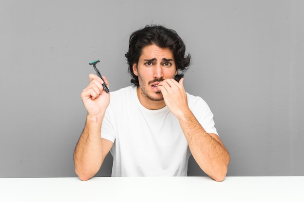 Joven sosteniendo una cuchilla de afeitar mordiendo las uñas, nervioso y muy ansioso.