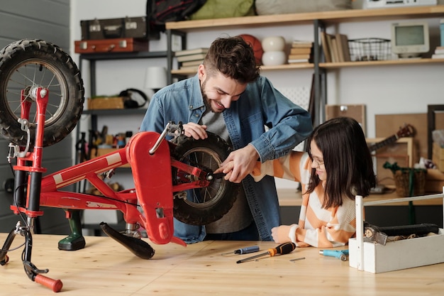 Joven sosteniendo la mano de su hija mientras revisa las ruedas de su bicicleta