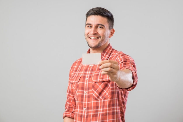 Joven sosteniendo y mostrando la tarjeta de visita en blanco aislada sobre fondo gris