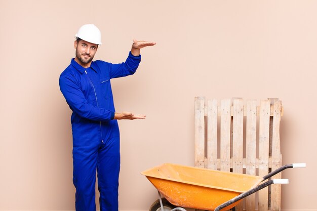 Joven sosteniendo un objeto con ambas manos en el espacio de copia lateral, mostrando, ofreciendo o publicitando un concepto de construcción de objetos