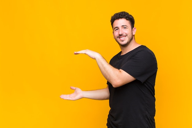 Joven sosteniendo un objeto con ambas manos en el espacio de copia lateral, mostrando, ofreciendo o publicitando un objeto