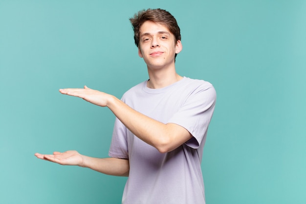 Joven sosteniendo un objeto con ambas manos en el espacio de copia lateral, mostrando, ofreciendo o publicitando un objeto