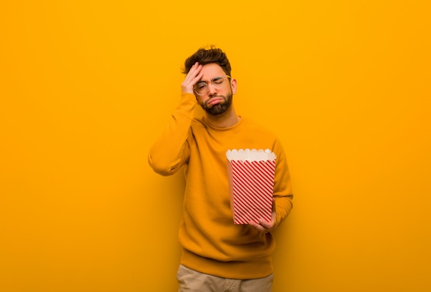 Joven sosteniendo palomitas cansado y con mucho sueño