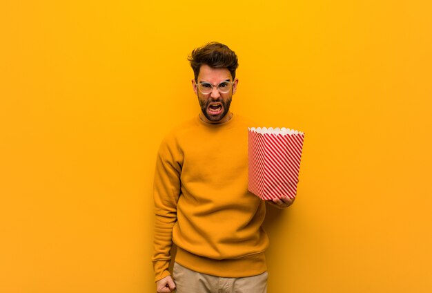 Joven sosteniendo palomitas gritando muy enojado y agresivo