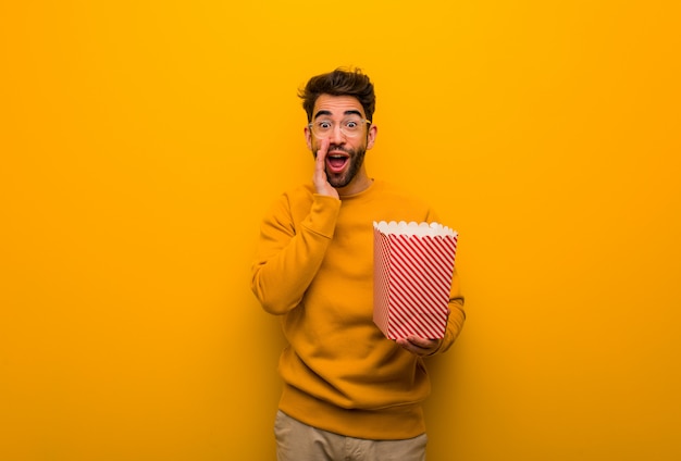 Joven sosteniendo palomitas de maíz gritando algo feliz al frente