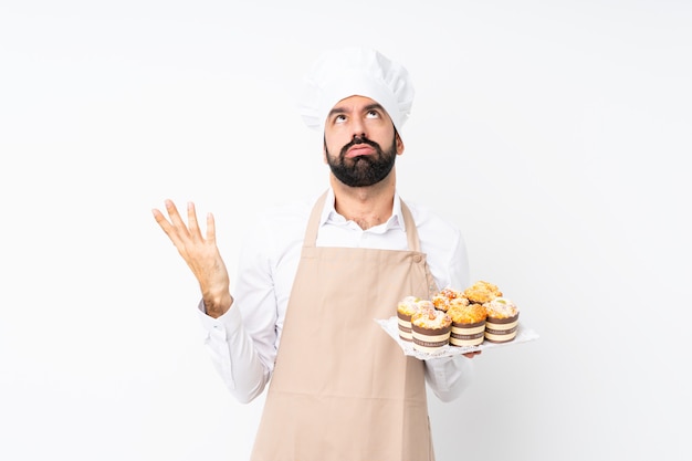 Joven sosteniendo pastel de muffin sobre pared blanca aislada frustrado por una mala situación