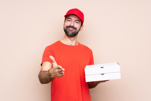 Joven sosteniendo una pizza estrechándole la mano para cerrar un buen trato