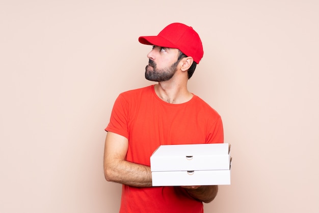 Joven sosteniendo una pizza sobre aislado con confundir expresión de la cara