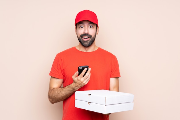 Joven sosteniendo una pizza sorprendido y enviando un mensaje