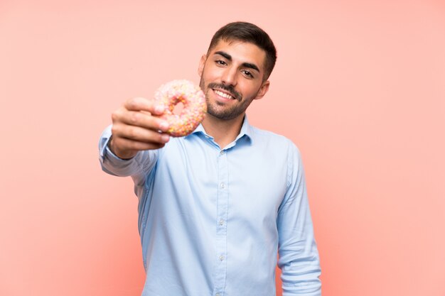 Joven sosteniendo una rosquilla sobre fondo rosa aislado