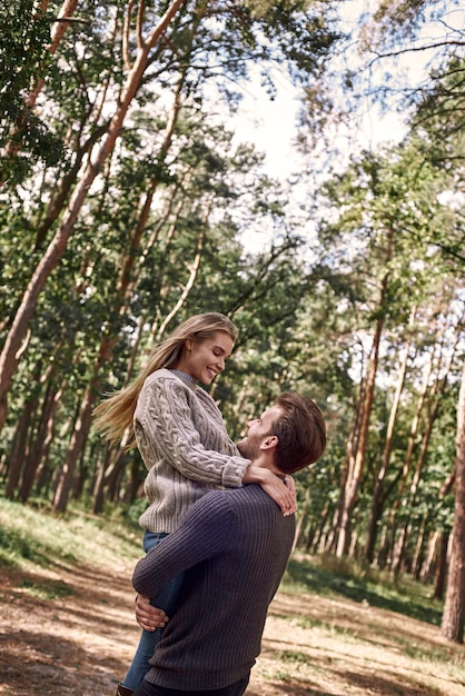 Joven sosteniendo a su novia en las manos en el bosque de otoño