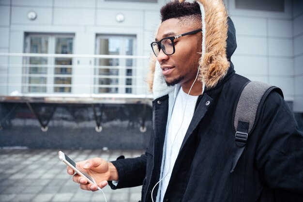 Joven sosteniendo su teléfono celular en las manos y charlando mientras escucha música.