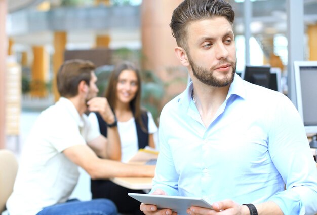 Joven sosteniendo tableta digital mientras sus colegas trabajan en segundo plano.