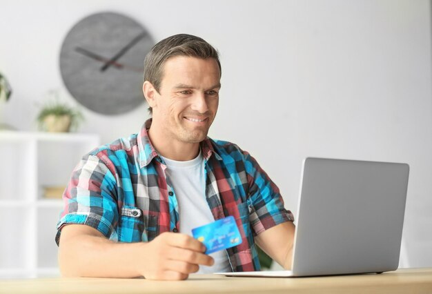 Joven sosteniendo la tarjeta de crédito mientras usa la computadora portátil en casa