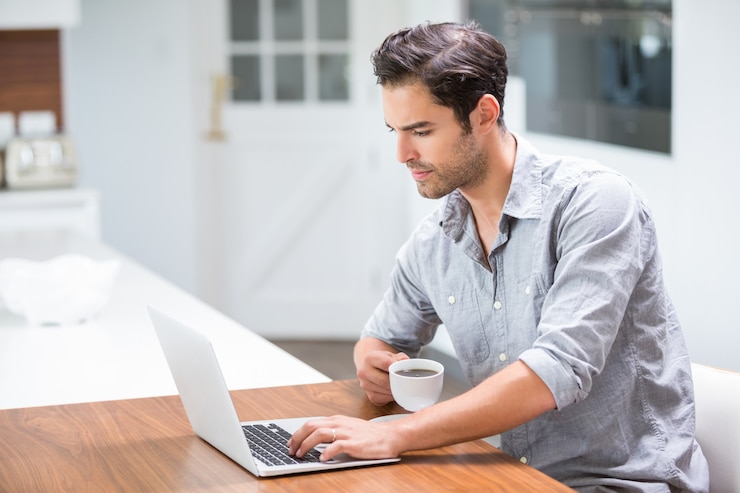 Foto joven sosteniendo la taza de café mientras trabajaba en la computadora portátil