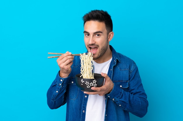 Joven sosteniendo un tazón de fideos sobre pared aislada