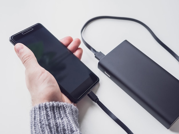 Joven sosteniendo un teléfono inteligente conectado a un banco de energía