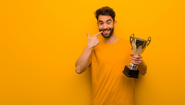 Joven sosteniendo un trofeo sonríe, señalando boca