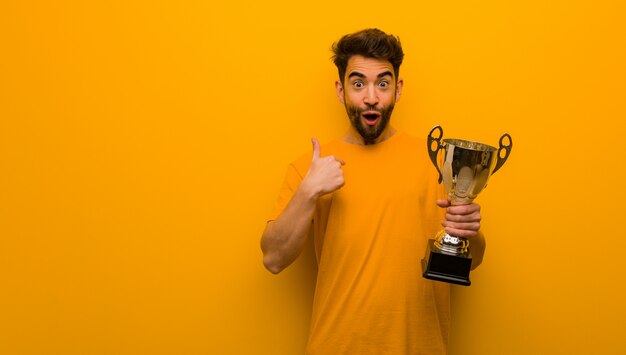 Joven sosteniendo un trofeo sorprendido, se siente exitoso y próspero