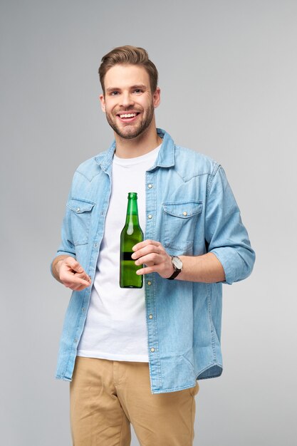 Joven sosteniendo vistiendo jeans camiseta sosteniendo una botella de cerveza de pie