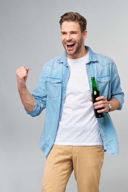 Joven sosteniendo vistiendo jeans camiseta sosteniendo una botella de cerveza de pie