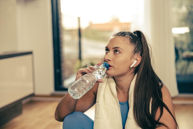 La joven sostiene una botella de agua y se prepara para entrenar en casa.